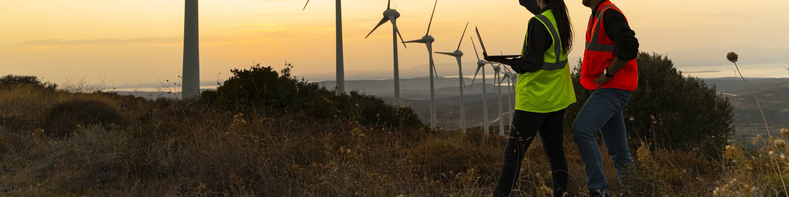 maintenance engineer team working in wind turbine farm at sunset